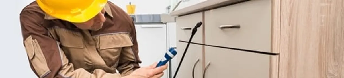 Roach exterminator applying treatment under kitchen cabinets in Detroit, MI