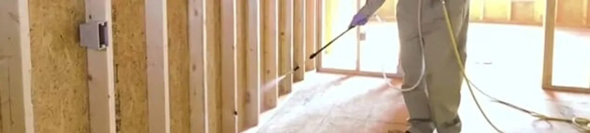 Termite treatment technician applying spray along framing and unfinished walls in Detroit, MI